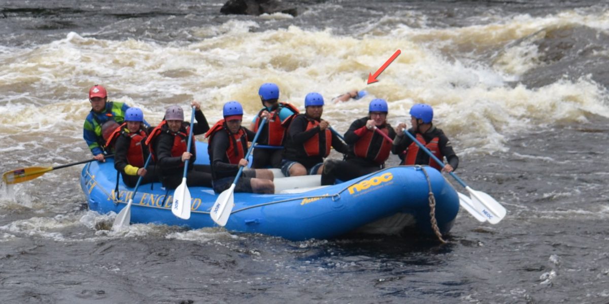 Image of a person floating in the rapids behind a raft with an arrow pointing to the person